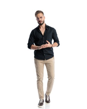 Gözlüklü sıradan bir genç, beyaz arka plan önünde yürüyor ve avuçlarını ovalıyor.