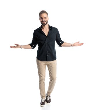 Gözlüklü gururlu genç adam gülümsüyor, ileriye bakıyor, kollarını açıyor ve beyaz arka planda yürüyor.