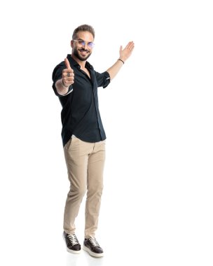 Sıradan bir sakallı adam gülümsüyor, başparmak işareti yapıyor ve beyaz arka planda dikilirken yan yana duruyor.