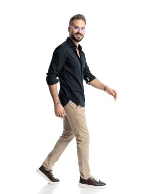 Gözlüklü, ileriye bakan ve beyaz arka planda yürüyen mutlu sıradan bir adamın yan görüntüsü.