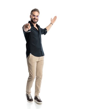 Gözlüklü mutlu sıradan bir adam, parmaklarını öne uzatıyor, gülümsüyor ve beyaz arkaplanın önüne davet ediyor.