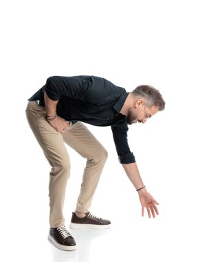 Gözlüklü sıradan bir gencin yan görünüşü öne eğilmiş ve beyaz arka planda yerden bir nesne alıyor.