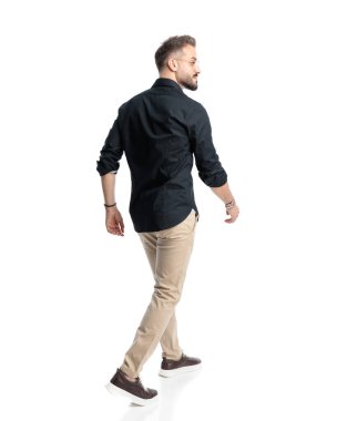 Gözlüklü genç adam beyaz arka planda yürürken gülümseyen ve yan yan bakan