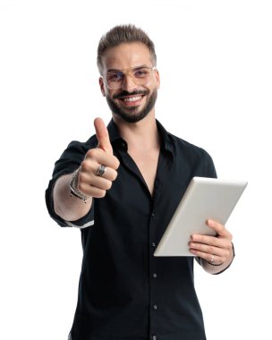 Gözlüklü, tabletli mutlu bir adam. Başparmak hareketi yapıyor ve beyaz arka planda gülümsüyor.