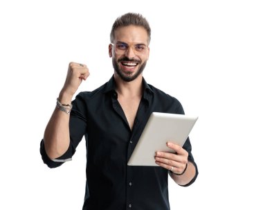 Gözlüklü, tabletli ve beyaz arka planda zaferi kutlayan heyecanlı sıradan bir adam.