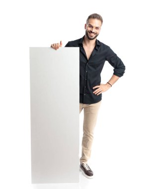 Gözlüklü mutlu genç adam boş tahtayı sunarken gülümsüyor ve beyaz arka planda duruyor.