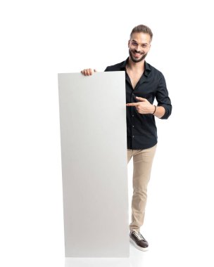 Gözlüklü, gülümseyen ve beyaz arka planda dururken boş tahtayı gösteren çekici, sıradan bir adam.