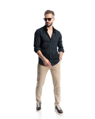 Güneş gözlüklü sıradan bir genç, el ele tutuşarak, yürür ve beyaz arka planın önüne bakar.