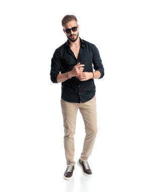 Havalı, güneş gözlüklü seksi adam ileriye bakıyor ve beyaz arka planda yürüyor.