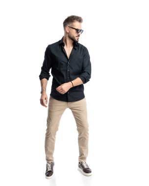 Güneş gözlüklü yakışıklı genç adam beyaz arka planın önünde duruyor.