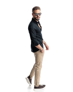 Güneş gözlüklü, el ele tutuşan ve beyaz arka planda yürüyen havalı moda adamının yan görüntüsü.