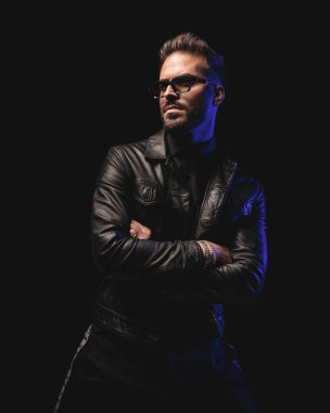 Güneş gözlüklü seksi adam siyah arka planda kollarını kavuştururken başka yöne bakıyor ve poz veriyor.