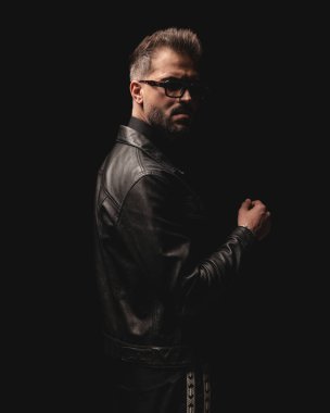 Güneş gözlüklü ve siyah arka planın önünde duran havalı genç adamın yan görüntüsü.