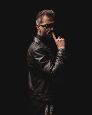 Güneş gözlüklü seksi adam dudaklarına dokunuyor ve siyah arka planda poz verirken sessizliğini koruyor.