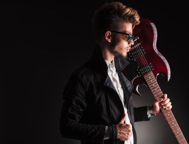 cool young guitarist holding his electric guitar on shoulder