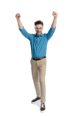 Gözlüklü mutlu genç adam, ayakta duruyor ve kutluyor iki yumruğu havada, beyaz arka planda izole..