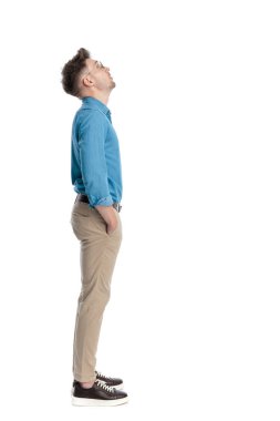 Gözlüklü, elleri ceplerinde duran ve beyaz arka planda izole edilmiş genç bir adamın yan görüntüsü..