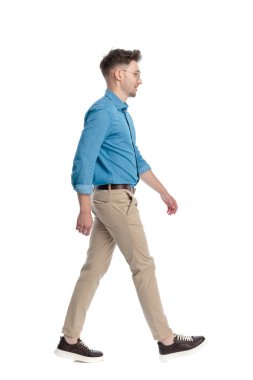 Gözlüklü, gülümseyen ve yürüyen, beyaz arka planda soyutlanmış mutlu genç bir adamın yan görüntüsü..