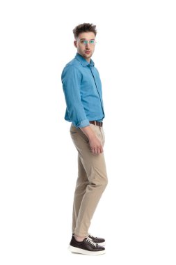 Gözlüklü, dikilip kameraya bakan, beyaz arka planda izole genç bir adamın yan görüntüsü..