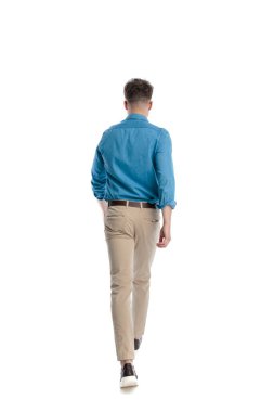 Mavi tişörtlü genç bir adamın arka planı. Bir eli cebinde, beyaz arka planda izole bir şekilde yürüyüp gidiyor..