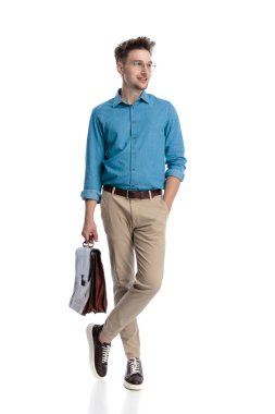 Gözlüklü ve çantalı, el ele tutuşmuş, bacakları çapraz duran, beyaz arka planda izole edilmiş, mutlu, genç bir adam..