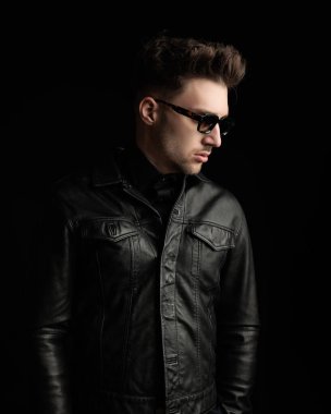 Siyah deri ceketli yakışıklı genç adam siyah arka planda poz veriyor. 