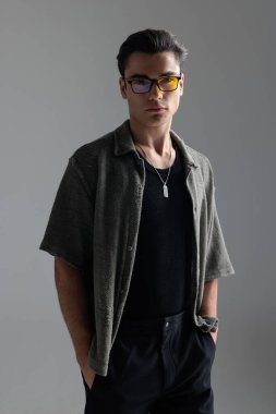 Gözlüklü, el ele tutuşan ve gri arka planda duran havalı moda adamı.