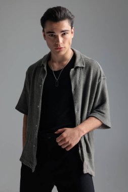 Gri hırkalı seksi genç adamın portresi ileriye bakıyor ve gri arkaplan önünde havalı bir şekilde poz veriyor.