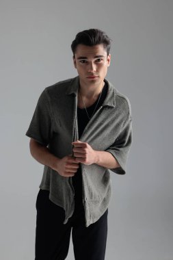 Çekici genç adam gri arkaplan önünde ileriye bakarken gri hırkayı dört gözle bekliyor ve ayarlıyor