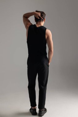 Siyah tişörtlü, arka planda elini başının arkasında tutan ve gri arka planda el ele duran havalı genç adam.