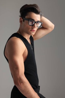 Gözlüklü, kafasının arkasında el ele tutuşan ve gri arka planda kaslarını gösteren seksi, formda adamın yan görüntüsü.