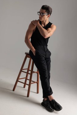 Gözlüklü, omuzlarına dokunan seksi kaslı adam. Gri arka planda el ele tutuşup yan tarafa bakıyor.