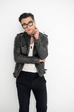 Siyah deri ceketli düşünceli genç adam tapınağa dokunuyor ve gri arkaplan önünde düşünüyor.