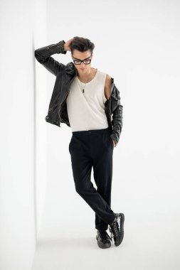 Kendine güveni tam, eli başının arkasında. Gri arka planın önündeki duvara bakıyor ve yaslanıyor.