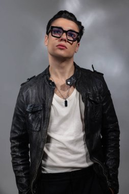 Siyah deri ceketli gözlüklü genç adam bulutların arkasında dikiliyor ve yukarı bakıyor.