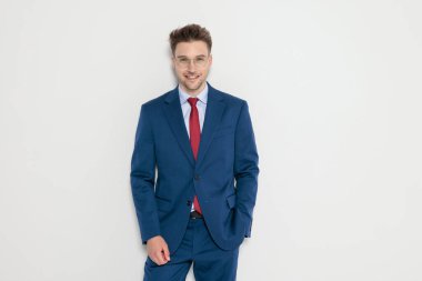 Mavi takım elbiseli ve gözlüklü mutlu zarif adam gülümsüyor. Gri arka planda tek eli cebinde duruyor.