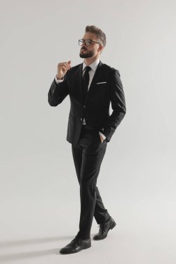 Takım elbiseli zarif çekici bir adam, cebinde bir el, gri arka planda yukarı bakıyor.