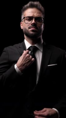 Ciddi, zarif bir adamın kravatını düzeltip karanlık stüdyonun arka planına bakarken çekilmiş dikey videosu..