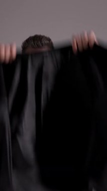 Güneş gözlüklü havalı adam ceketini giyiyor ve gri stüdyo geçmişiyle uzaklaşıyor..