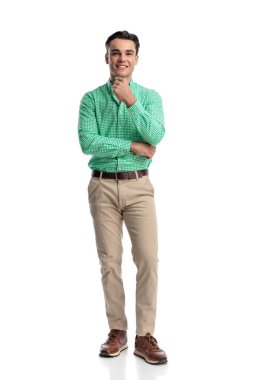 Mutlu genç adam, beyaz arka planda yalnız başına ileriye bakarken çenesine dokunup gülümsüyor.