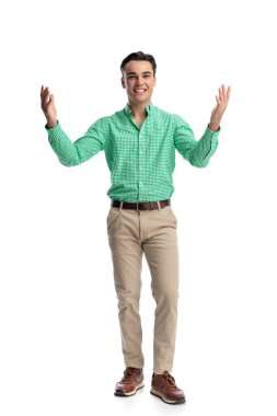 Hevesli genç adam beyaz arka planda durup ileriye bakarken kollarını ardına kadar açıyor.