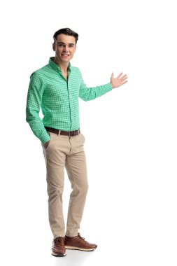 Dost canlısı genç erkek, şık giyinmiş, ayakta duruyor ve beyaz arka planda tek başına ileriye bakarken el kol hareketi yapıyor.