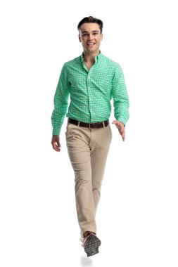 Beyaz arka planda, kendinden emin bir gülümsemeyle yürüyen mutlu, sıradan bir genç adam.