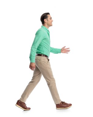 Beyaz stüdyonun arka planında yürüyen ve ileriye bakan neşeli genç bir adam.