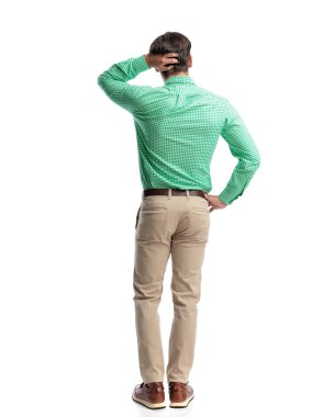 Kafası karışmış yeşil kareli gömlekli ve bej pantolonlu bir adamın beyaz arka planı düşünürken kafasını kaşıması.