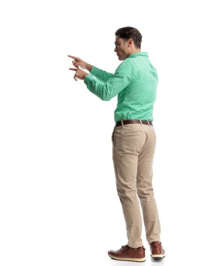 Yeşil kareli gömlekli ve bej pantolonlu beyaz arka planı işaret eden odaklanmış adamın yan görüntüsü