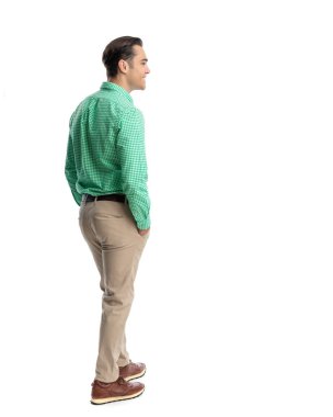 Yeşil kareli gömlek ve bej pantolon giyen, elleri ceplerinde beyaz arka plana bakan neşeli bir adamın yan görüntüsü.