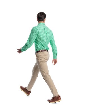 Arkadaki görüntüde yeşil ekose gömlek ve beyaz arka planda bej pantolon giyen sıradan bir adam sola doğru yürüyor.