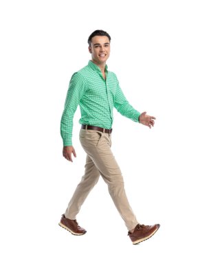 Yeşil ekose gömlekli neşeli genç adam beyaz arka planda ilerlerken yürüyor ve gülümsüyor.