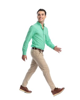 Yeşil kareli tişört giyen mutlu genç adam beyaz arka plana bakarken yürüyor ve gülümsüyor.